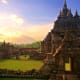Ancient Hindu temple with multiple stone spires at sunset in Indonesia, visitors exploring historic ruins with green fields a